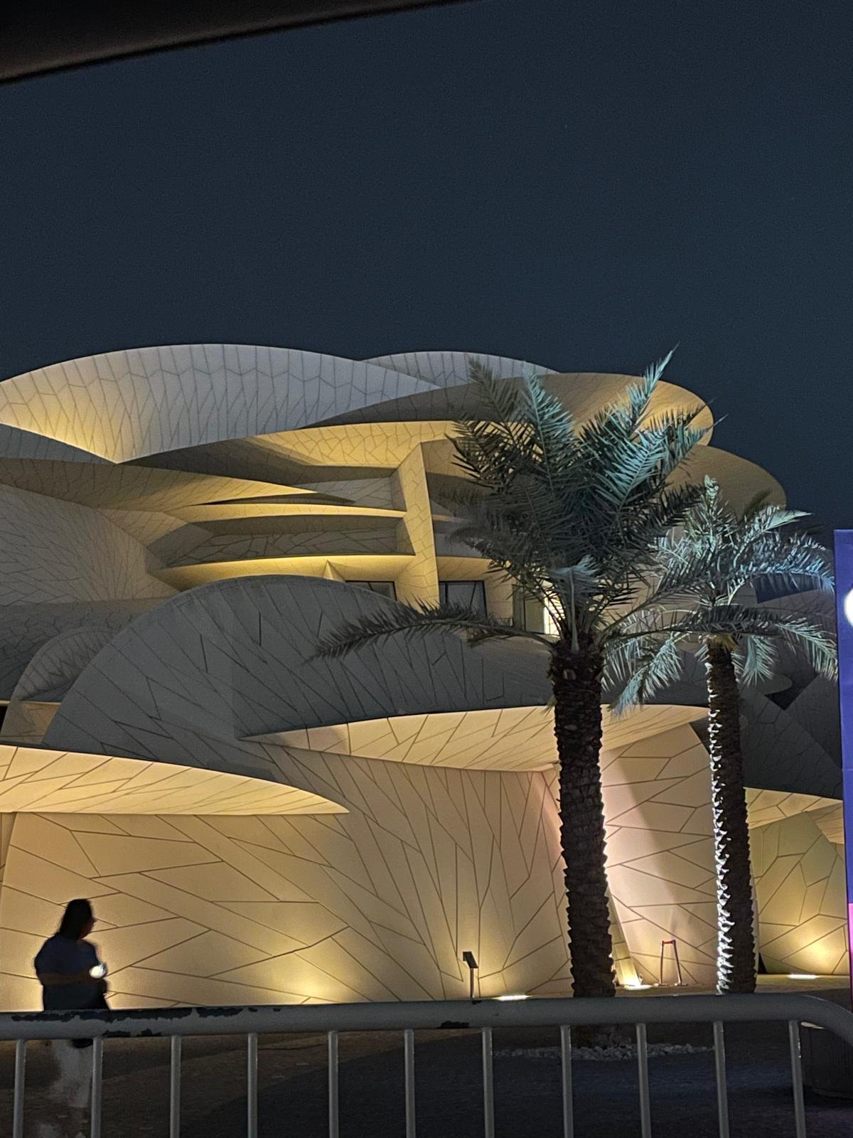 The National Museum of Qatar lit at night behind palm trees