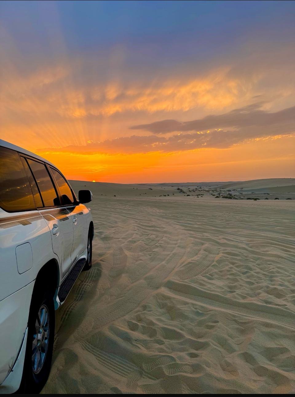A Land Cruiser on the sand with the sun setting behind the dunes